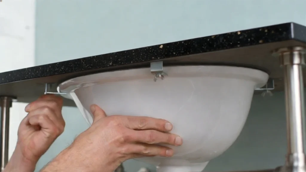 Professional undermount sink installation on granite using epoxy and metal clips for a permanent mechanical bond in hotel bathrooms.