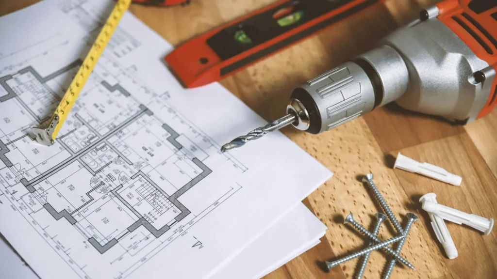 Professional blueprints with measuring tools and a power drill for verifying custom vanity dimensions and site plumbing.