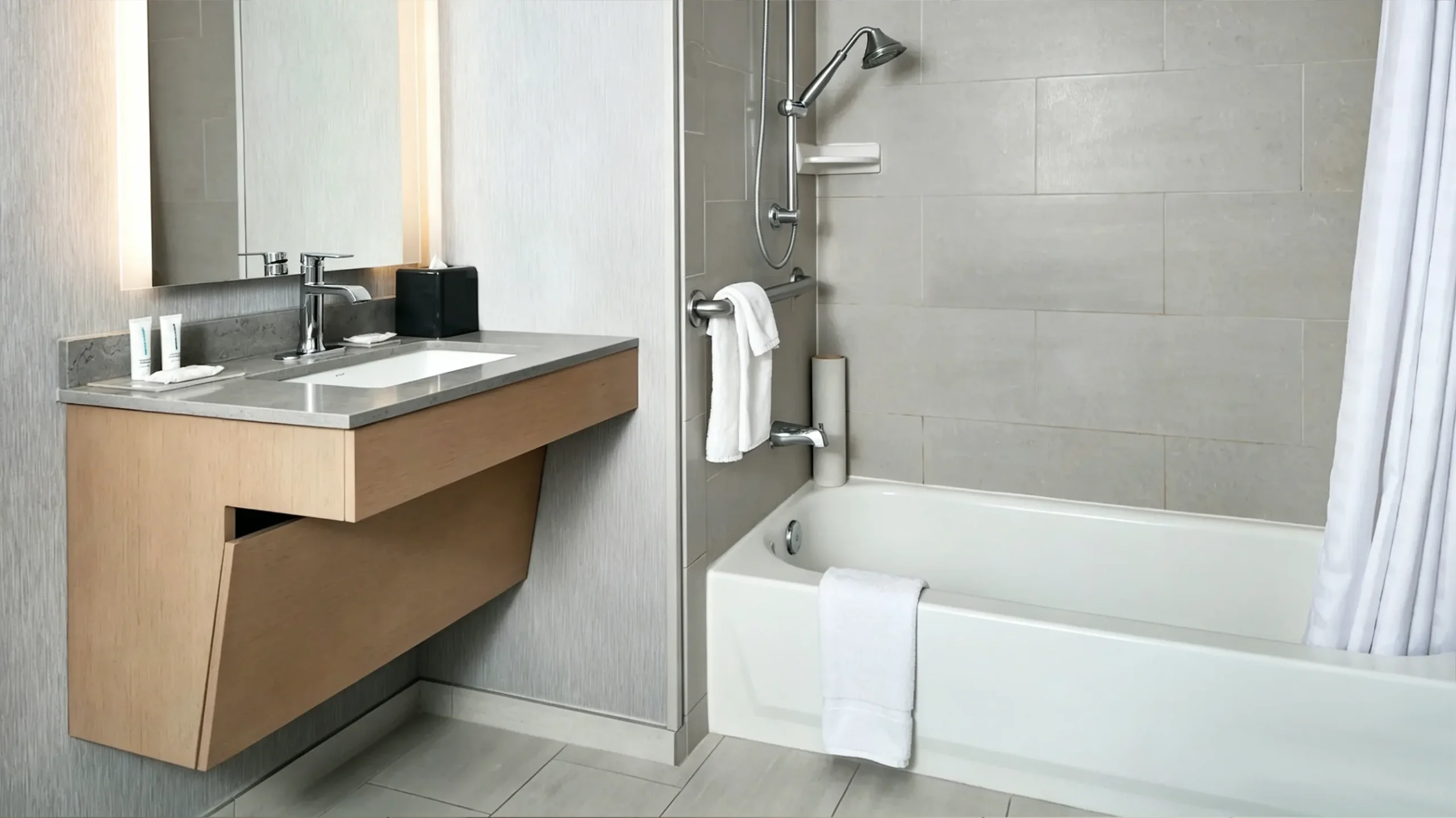 ADA-compliant light wood hotel vanity with slanted knee clearance for wheelchair access and integrated quartz countertop.
