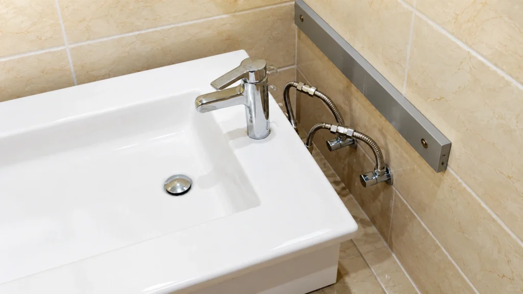 Exposed plumbing and metal wall support bracket for a white ceramic floating vanity installation in a commercial bathroom.
