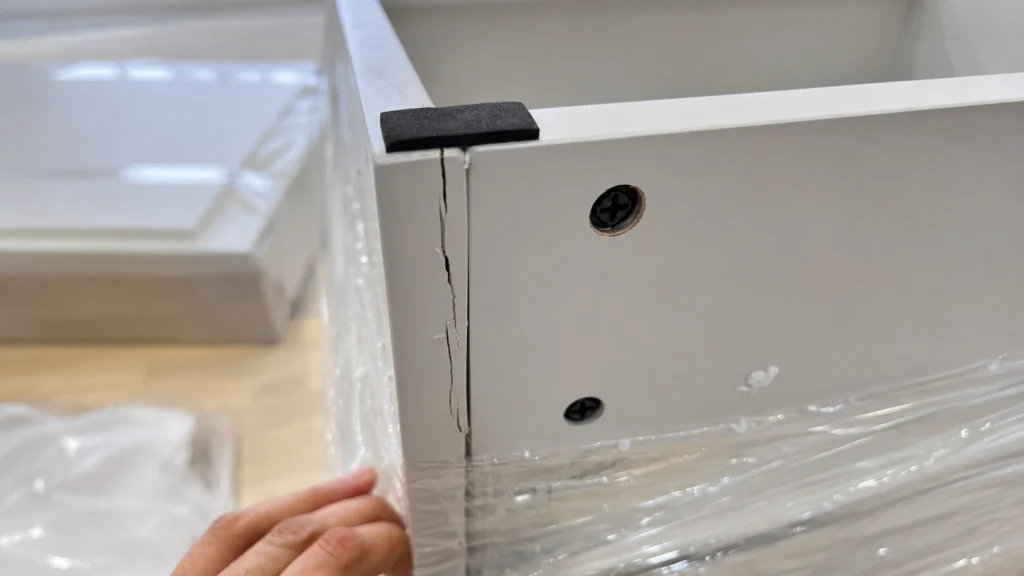 Cracked corner on a white Shaker bathroom cabinet box showing material failure during a B2B project quality inspection.