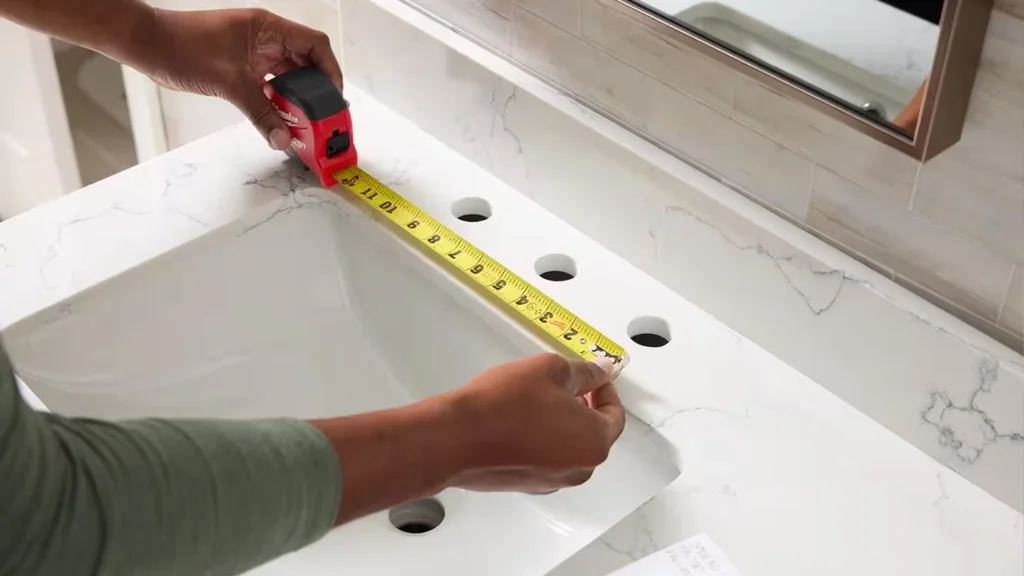 Measuring faucet hole spacing on a white marbled vanity top to ensure precise plumbing fit for hotel bathroom projects.
