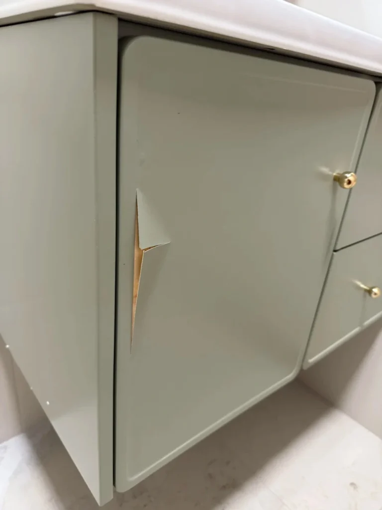 Peeling sage green paint on a hotel vanity door, showing finish adhesion failure and poor coating durability.