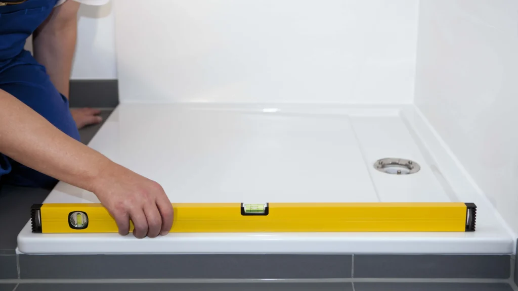Installer checking threshold level of an acrylic shower tray with a yellow spirit level during bathroom construction.