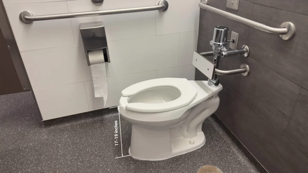 White elongated toilet in a hotel bathroom project, marked with a 17-19 inch seat height measurement for ADA compliance.
