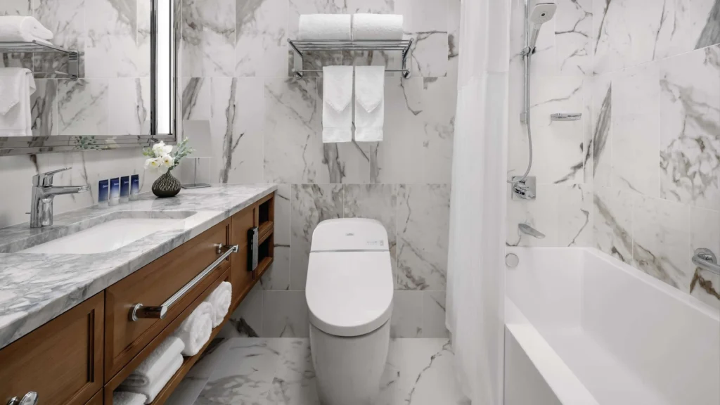 White integrated smart bidet toilet installed in a luxury marble hotel suite bathroom beside a wooden vanity.