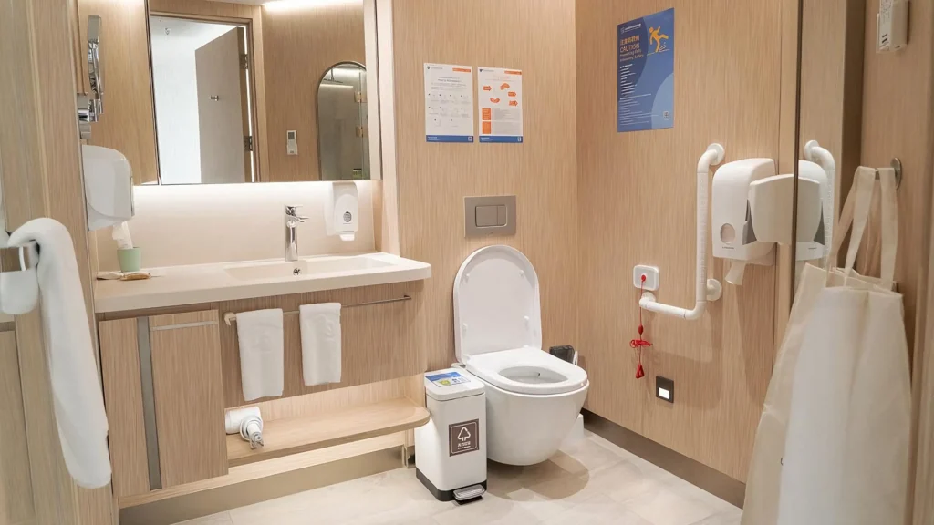 Accessible white wall-hung toilet with safety grab bar and emergency pull cord in a healthcare restroom.