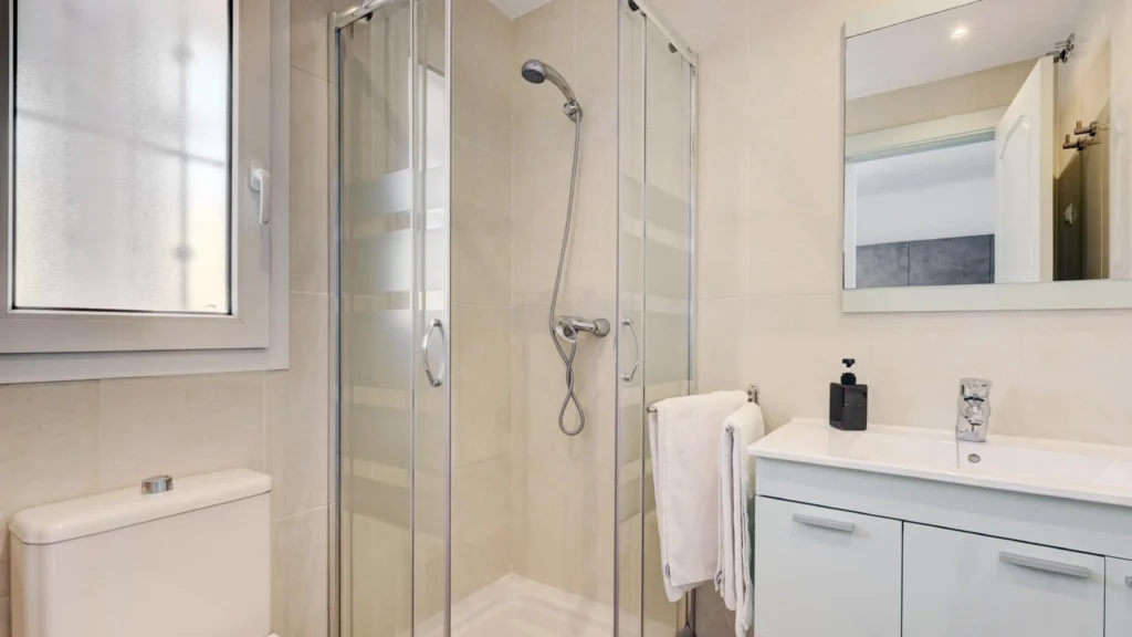 Chrome corner-entry sliding shower door with frosted glass in a compact hotel bathroom flanked by toilet and vanity.