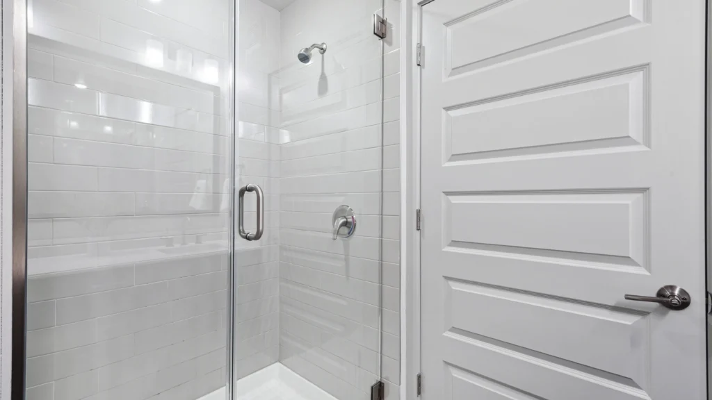 Modern apartment bathroom featuring a durable glass hinged shower door with sleek chrome hardware, showcasing standard multi-unit design.