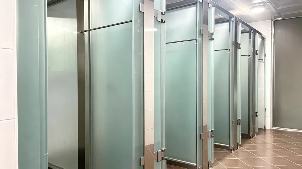 Standardized row of durable frosted glass shower partitions for low-maintenance privacy in large multifamily housing project bathrooms.