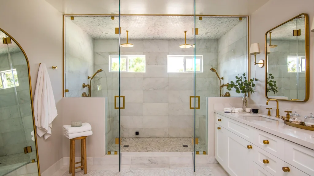 Clear glass shower doors showcasing marble wall tiles and brushed brass fixtures in a luxury hotel bathroom.
