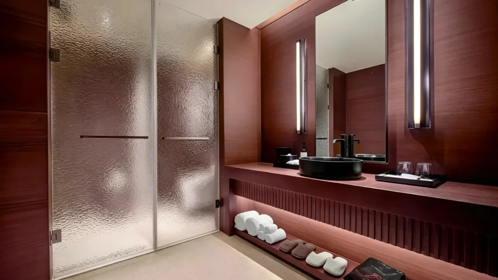 Textured rain glass shower doors beside a dark wood vanity, offering privacy in an upscale hotel guest bathroom.