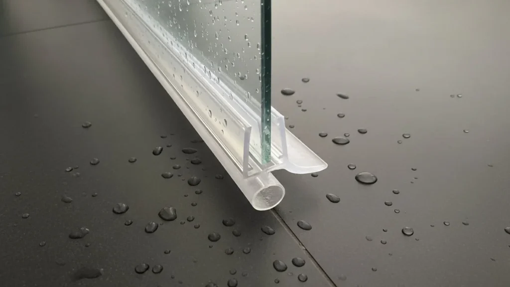 Continuous clear vinyl sweep on a hinged glass shower door preventing water leaks along the bottom threshold.
