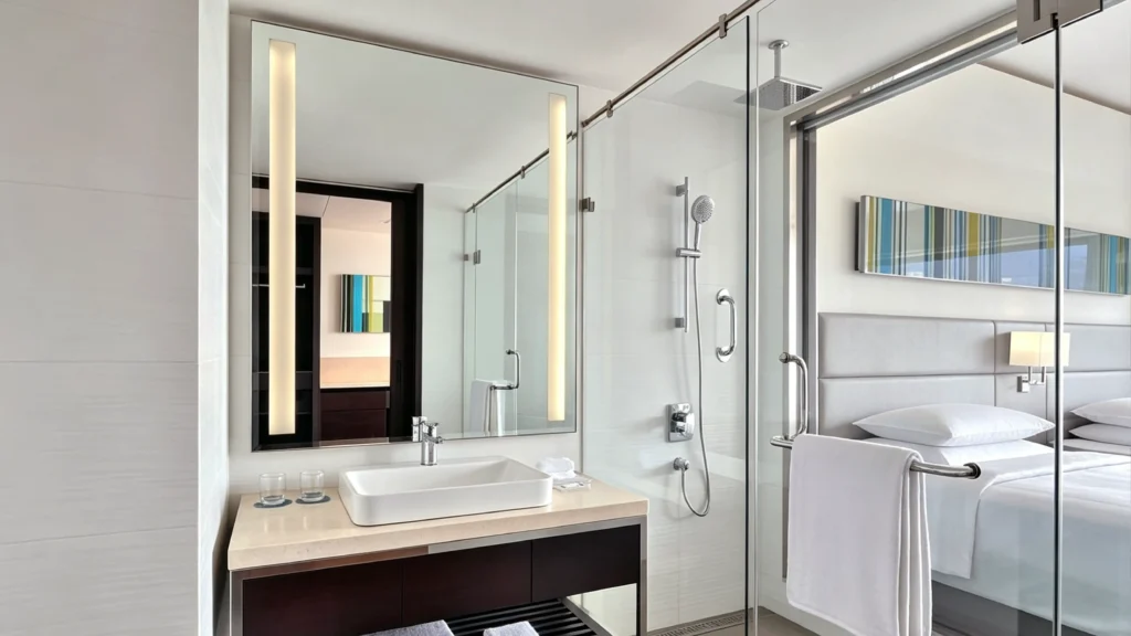 Standardized sliding glass shower door with chrome hardware in an open-concept hotel guest room bathroom.